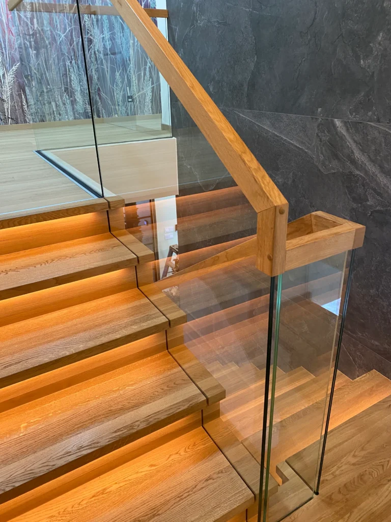Detailaufnahme einer modernen Holztreppe mit integrierter Beleuchtung und Glasgeländer. Die Treppe ist eine Maßanfertigung und besticht durch ihr elegantes Design. Ideal für den individuellen Treppenbau.