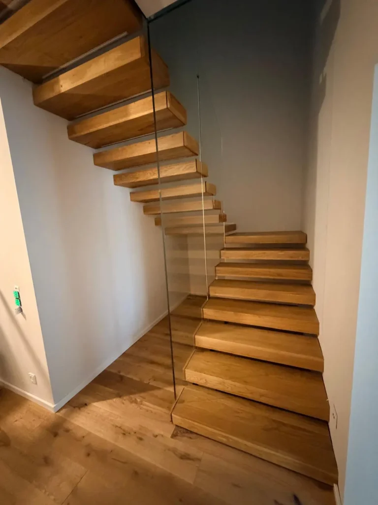 Freitragende Holztreppe mit Glaswange und hellen Holzstufen. Die Treppe ist modern und minimalistisch gestaltet und führt in einem hellen Raum nach oben. Maßanfertigung für individuelle Wohnraumgestaltung.